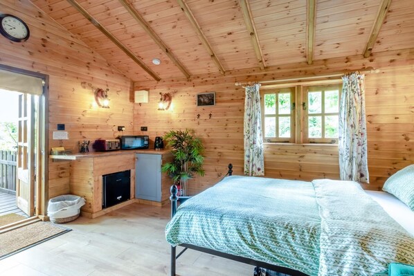 Une cabane en bois avec un lit, une petite cuisine et une fenêtre avec des rideaux.