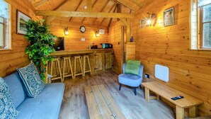 Ein gemütliches Blockhauskamin-Interieur mit Holzbalkendecke, einer Bar, einer Couch, einem Sessel und einem Esstisch.