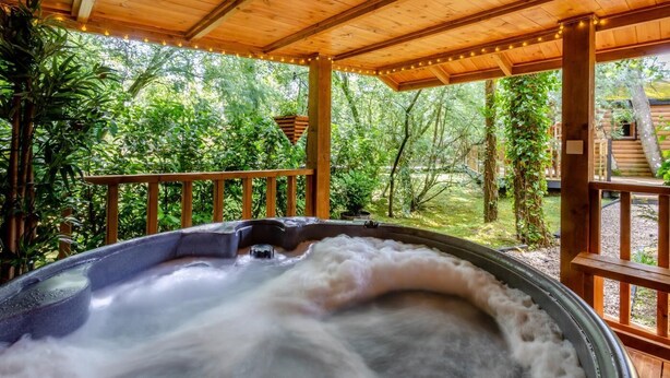 Ein Whirlpool unter einer Holzpergola mit Blick auf eine bewaldete Landschaft.