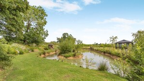 Ein Rasen mit einem Teich, Bäumen und einem Pavillon.