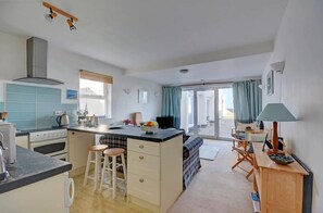 Eine Küche mit Kochinsel, zwei Barhocker, einem Essbereich mit Tisch und Stühlen sowie Blick durch eine Glastür.