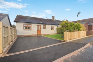 Une maison de plain-pied avec une porte d’entrée, deux fenêtres, une allée pavée et une clôture en bois.