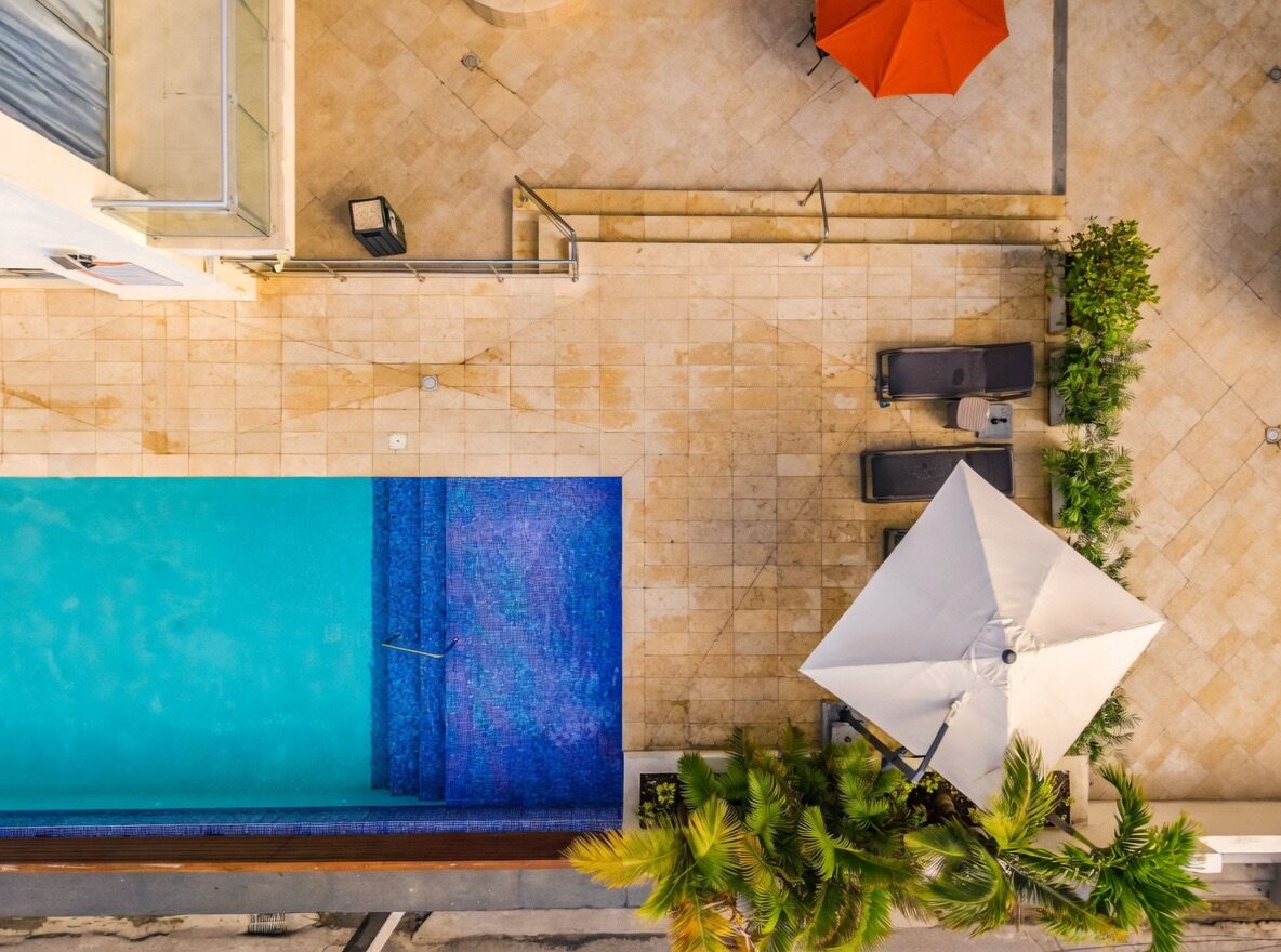 Ein Blick von oben auf einen Poolbereich auf einem Dach, mit einem blauen Pool, einem weißen Sonnenschirm und Sitzgelegenheiten.