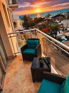 Ein Balkon mit Korbmöbeln und Blick auf den Sonnenuntergang über dem Meer.