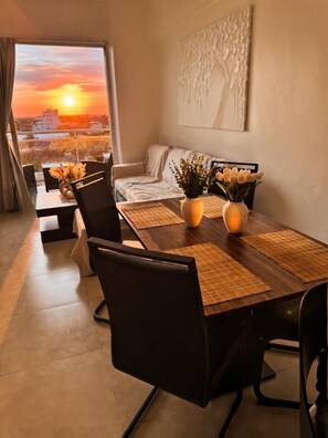 A dining area with a view of a sunset, a sofa, and a painting on the wall. - 2- Bedroom Skyrise apartment in Stunning Boca Chica with Breathtaking Oceanview. (Boca Chica)