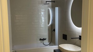 Ein modernes Badezimmer mit einer Duschkabine, einem weißen Waschbecken und einem großen Spiegel.