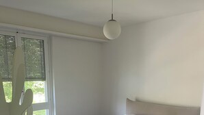Ein Schlafzimmer mit Bett, Holzboden, einem Fenster mit Jalousien und einer Pendelleuchte.