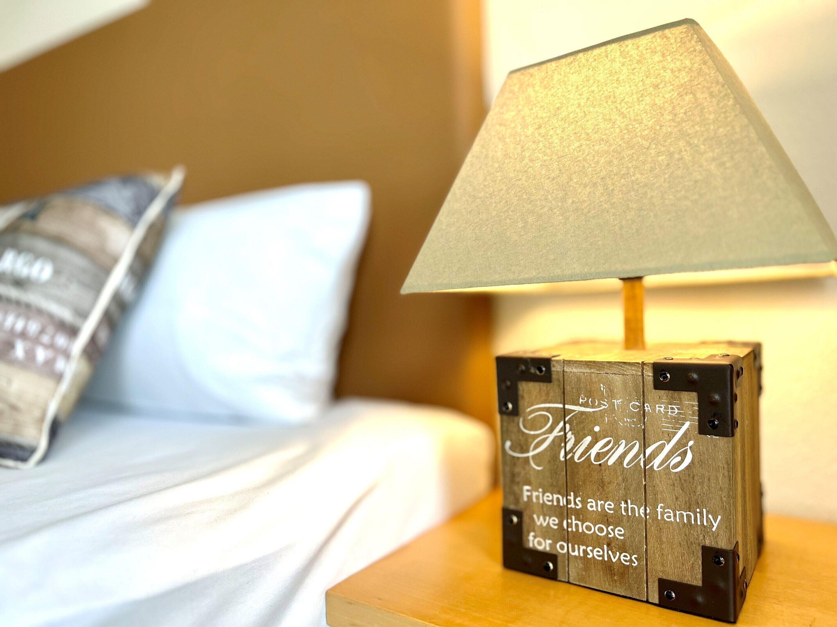 A wooden block with 'Friends' and a quote on a bedside table with a lamp.