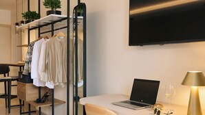 A modern hotel room with a desk, chair, TV, and a plant. - Urban Residence: Stylish comfort with city views in the heart of Piraeus. (Pireas)