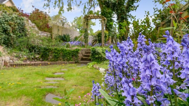 A garden with a stone pathway, flowering plants, and a wooden pergola. - 2 Bed in Kingsteignton (oc-w34194) (Kingsteignton)