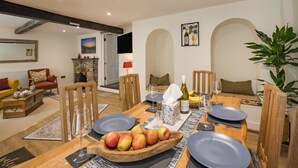 A dining area with a wooden table set for four, a fruit bowl, wine glasses, and a bottle. - 2 Bed in Kingsteignton (oc-w34194) (Kingsteignton)