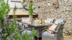 An outdoor dining area with wicker furniture and a glass table, set against a stone wall. - 2 Bed in Kingsteignton (oc-w34194) (Kingsteignton)