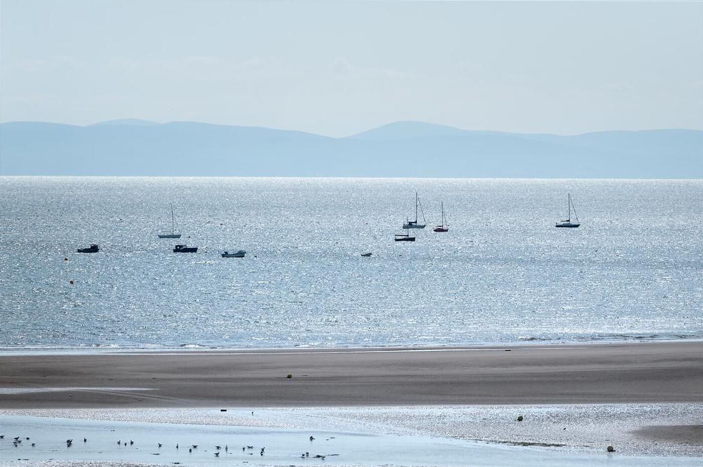 A beach with boats on the water and a sandy shore.