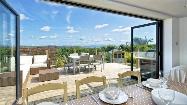 Ein Essbereich mit Tisch für zwei Personen, mit Blick auf eine Terrasse, die Sitzmöglichkeiten im Freien und eine schöne Aussicht bietet.