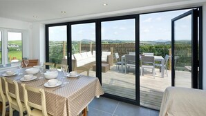 Ein Essbereich mit Tisch für vier Personen, einer Couch und Blick auf eine Terrasse mit Gartenmöbeln.