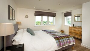 Ein Schlafzimmer mit Bett, Nachttisch, Lampe, Kommode und Fenstern.