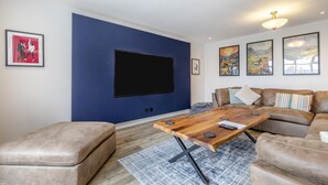 Ett vardagsrum med en stor TV med platt skärm, ett soffbord i trä, lädersoffor och en mönstrad matta.