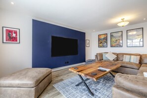 Ein Wohnzimmer mit großem Flachbildfernseher, einem Holztisch, Ledersofas und einem gemusterten Teppich.
