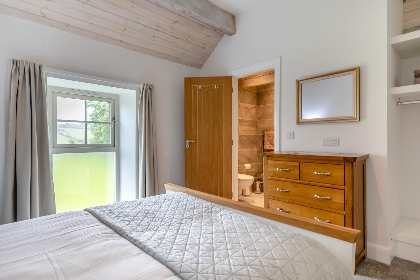 A bedroom with a bed, wooden wardrobe, and a window with curtains.