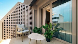 Ein Balkon mit weißem Tisch und Stuhl, Blumentöpfen und Blick auf ein Gebäude.