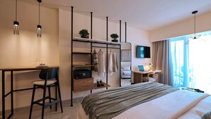 Ein Hotelzimmer mit Bett, Schreibtisch mit Stuhl, Fernseher, Kleiderschrank und einem Fenster mit Vorhängen.