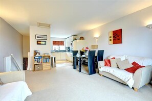 A modern living room with a white sofa, a dining area with a table and chairs, and a kitchen in the background. - 2 Bed in Saundersfoot (oc-pw516a) (Saundersfoot)