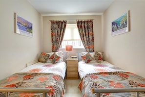 A bedroom with two single beds, a window with curtains, a bedside table, and a lamp. - 2 Bed in Saundersfoot (oc-pw516a) (Saundersfoot)