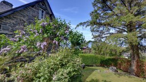 A stone building with a sloped roof, a large tree, and a well-maintained garden. - 2 Bed in Harlech (oc-wah467) (Harlech)