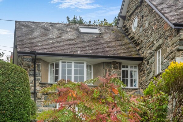 Une maison en pierre avec un toit en pente, une baie vitrée et une petite lucarne.