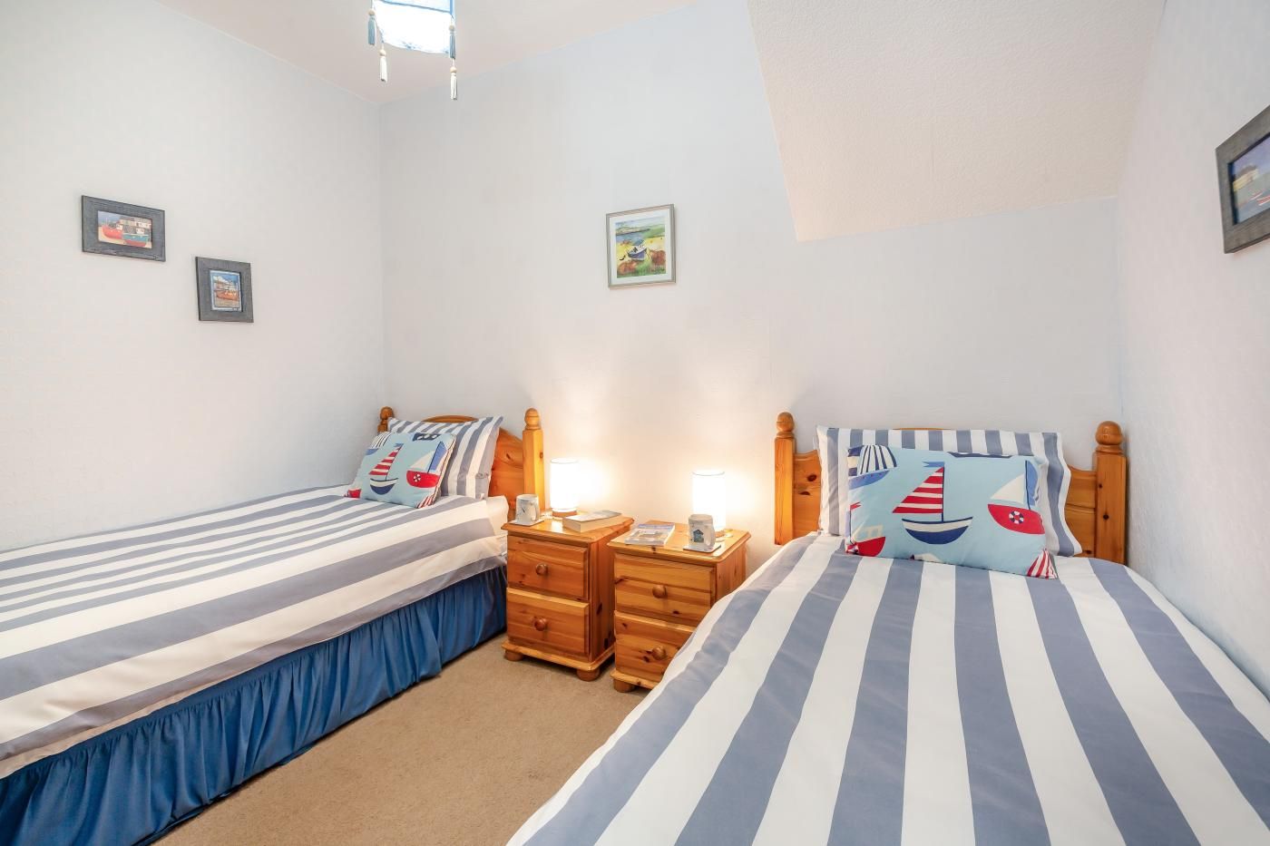 A bedroom with two single beds, each with a wooden headboard, a bedside table, and a lamp.