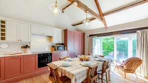 A kitchen with white and pink cabinets, a dining table set for four, and a view of greenery outside. - 3 Bed in Bamburgh (oc-t34385) (Bamburgh)