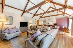 A spacious living area with a high ceiling, wooden beams, a sofa set, a television, and a kitchen in the background. - 3 Bed in Bamburgh (oc-t34385) (Bamburgh)