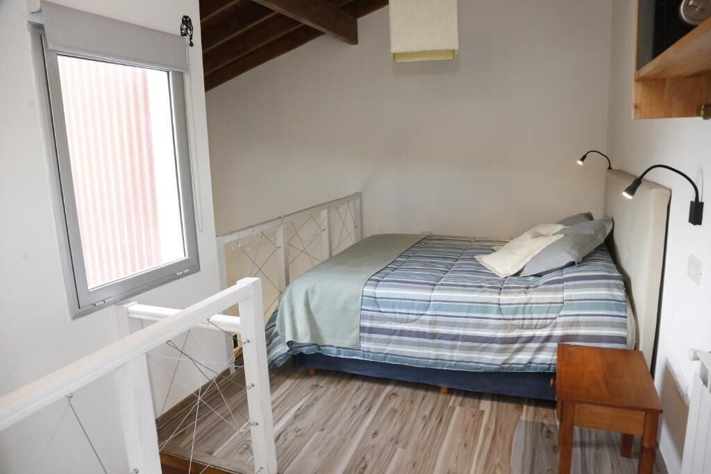 A bedroom with a bed, a window, a desk, and a lamp.