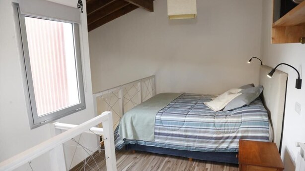 A bedroom with a bed, a window, a desk, and a lamp.