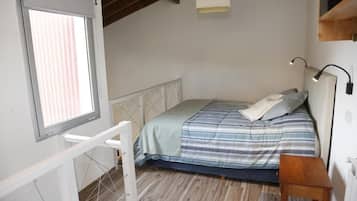 A bedroom with a bed, a window, a desk, and a lamp.