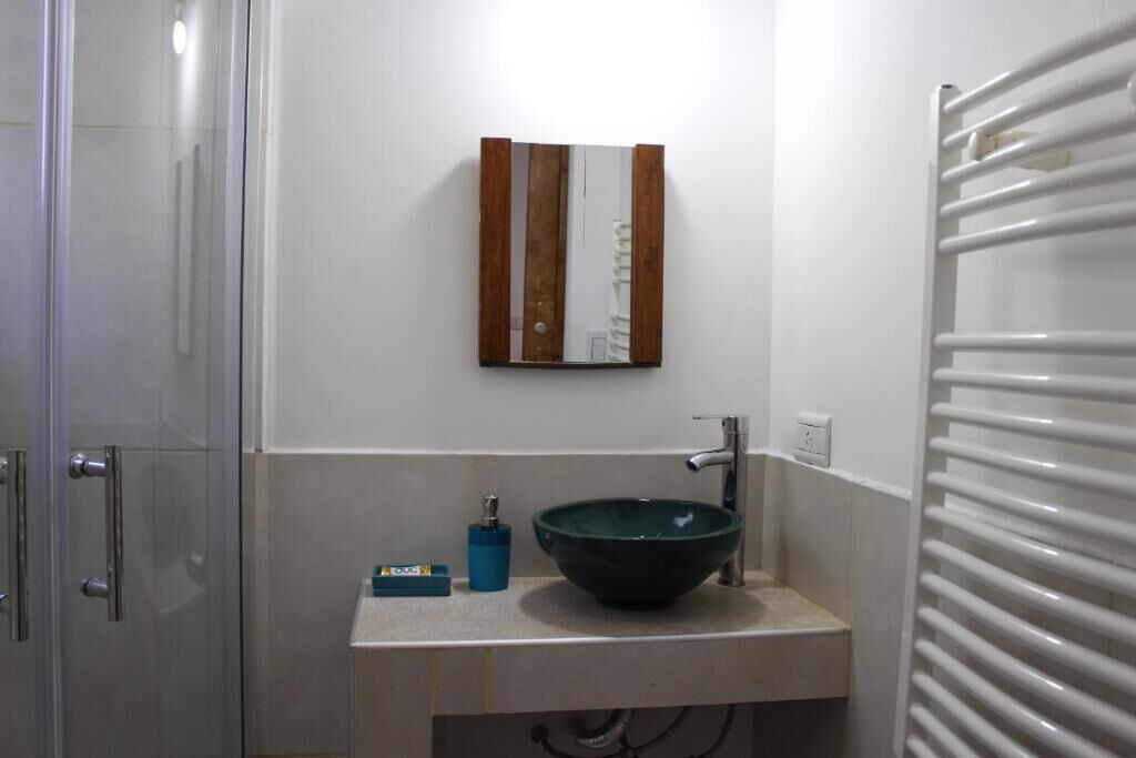 Casa de banho com cabine de duche em vidro, lavatório com cuba verde e porta-toalhas.