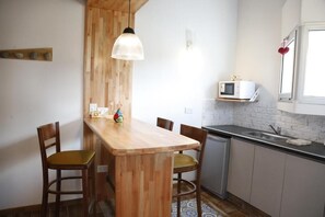 Una cuina amb una illa de fusta, cadires, una llum penjant, microones i un rentaplat.
