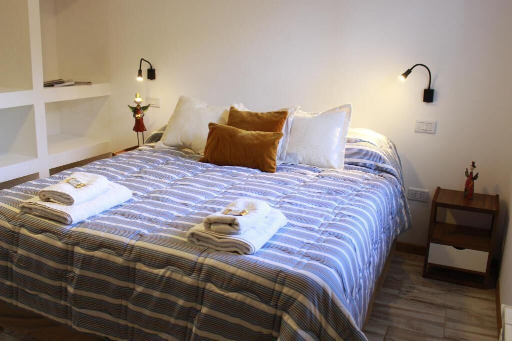 A neatly made bed with striped bedding, two bedside lamps, and a small wooden nightstand with a decorative item.