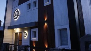 Un bâtiment moderne à deux étages, doté d’un logo bien visible sur la façade, de marches en pierre menant à l’entrée et d’une façade bien éclairée.