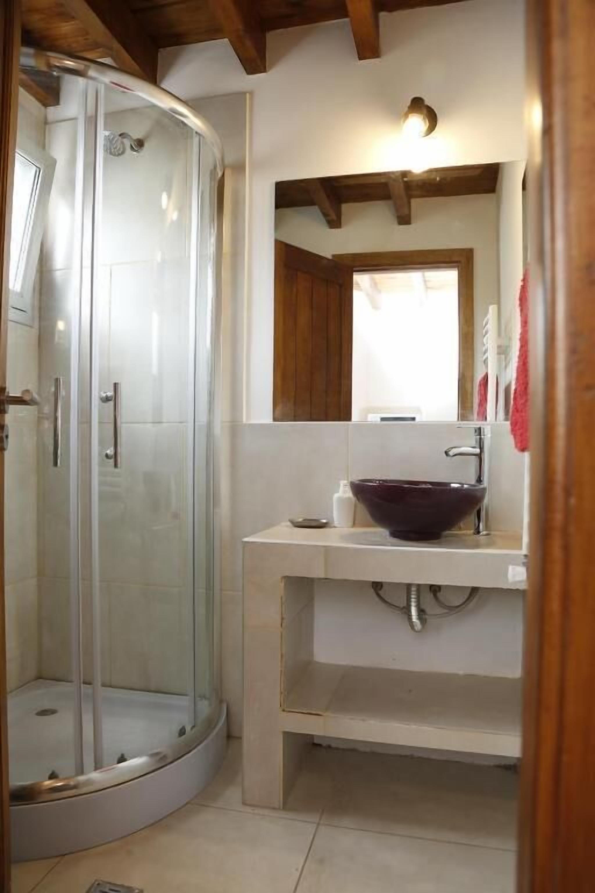 Un baño con cabina de ducha de vidrio, un lavabo blanco con un recipiente grande y un techo de madera.