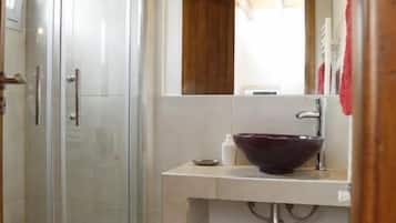 Un baño con cabina de ducha de vidrio, un lavabo blanco con un recipiente grande y un techo de madera.