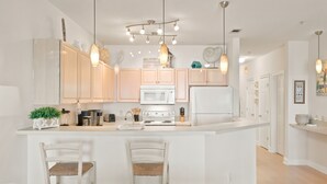 A modern kitchen with white cabinetry, a central island with bar stools, and pendant lighting. - Welcome to Rivieria Dunes #102 (Perdido Key)