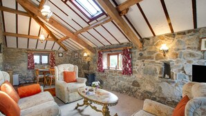 Un intérieur rustique avec des murs en pierre, des poutres en bois, une cheminée en pierre et un coin repas comprenant une table et des chaises.