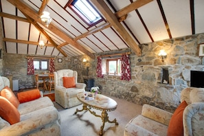 Ein rustikales Interieur mit Steinwänden, Holzbalken, einem Steinofen und einer Essecke mit Tisch und Stühlen.