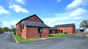 A brick building with a sloped roof, a paved driveway, and a grassy area in front. - 1 Bed in Llandinam (oc-waa376) (Llandinam)