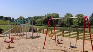A playground with swings, slides, and climbing structures. - 1 Bed in Llandinam (oc-waa376) (Llandinam)