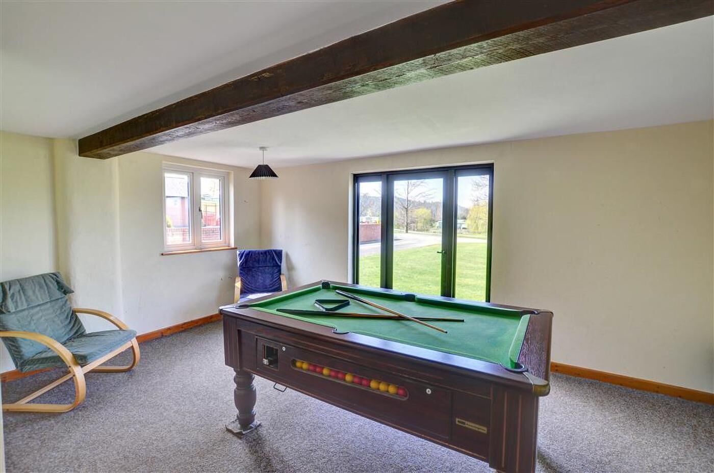 A pool table in a room with a window, a chair, and a ceiling beam.