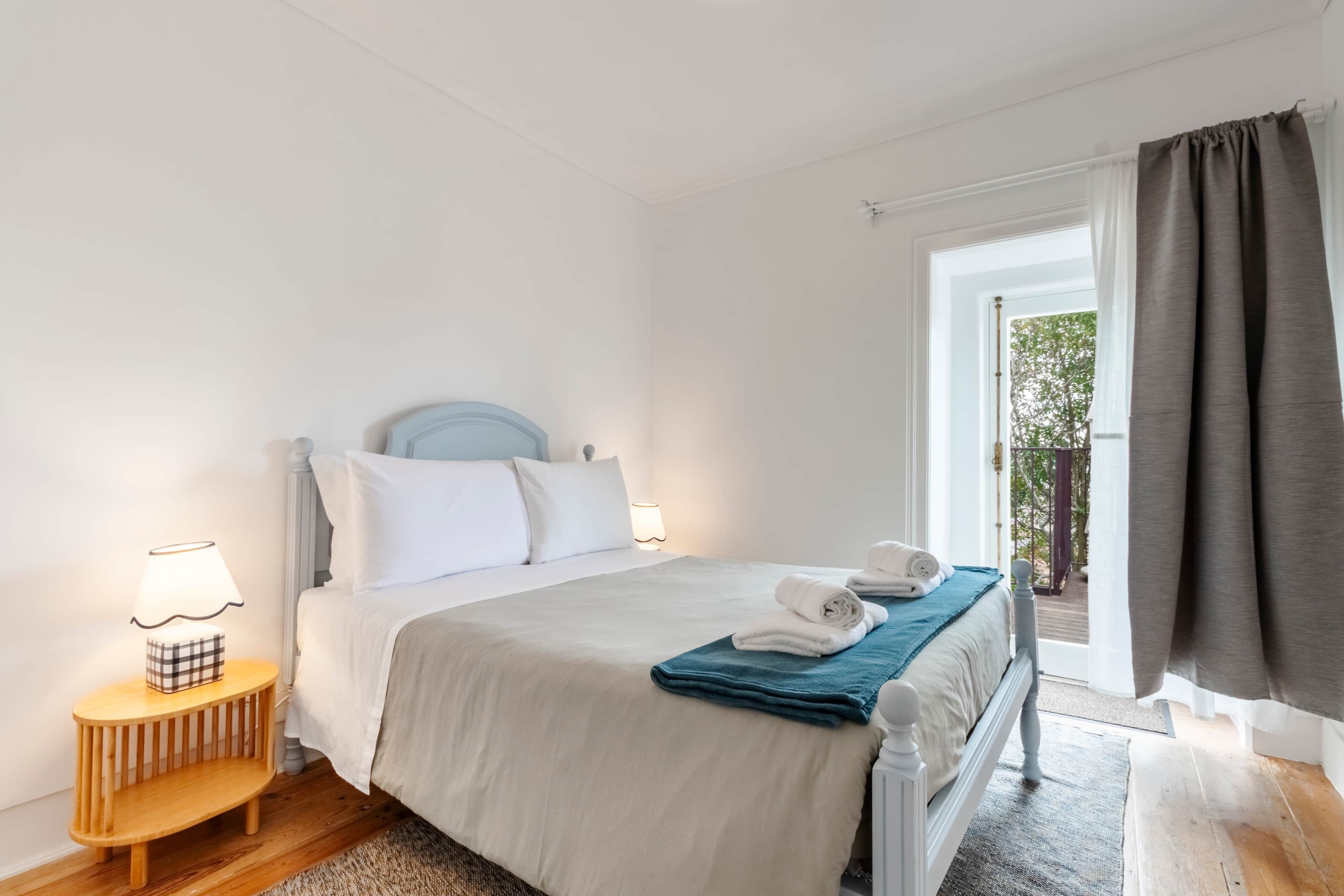 Ein Schlafzimmer mit Bett, Nachttischlampe und Blick ins Freie.
