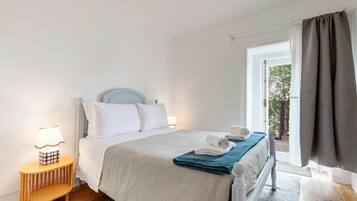 A bedroom with a bed, bedside lamp, and a view of the outdoors.