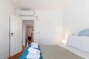 A hotel room with a bed, a blue towel, a white door, and a hallway leading to another room. - Panorama View Apartment in Amazing Viewpoint (Lisbon)